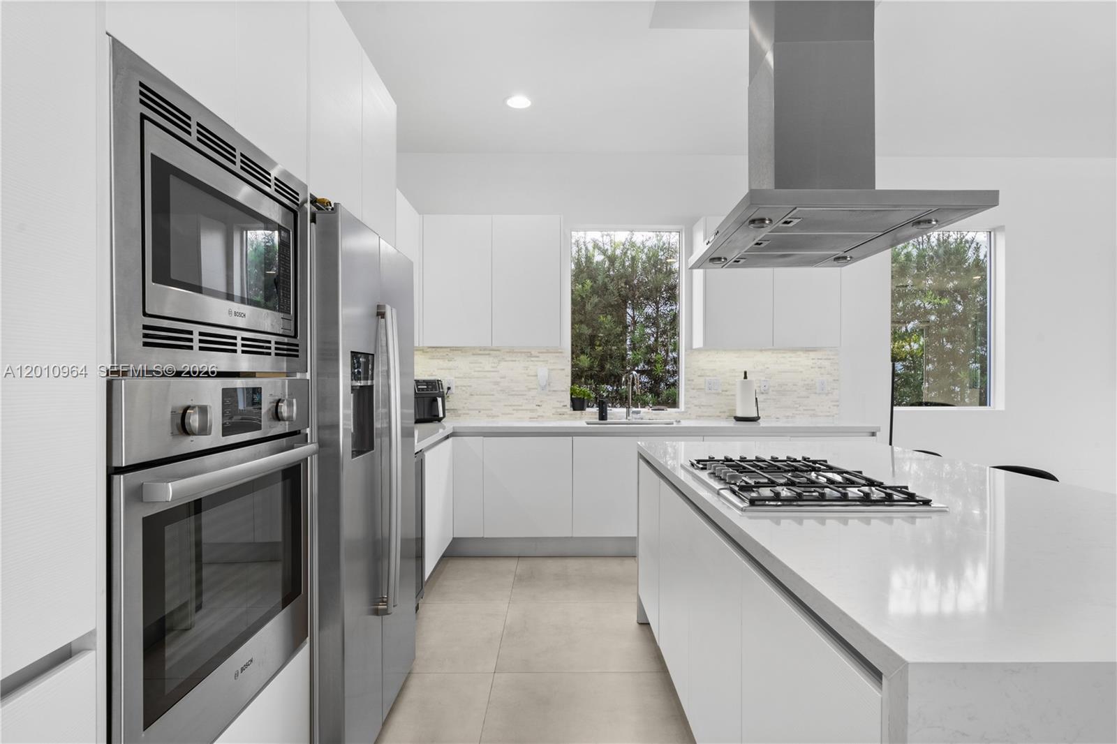 A modern white kitchen features stainless steel appliances, a center island, and large windows — 9915 NW 75th St # 9915, Doral FL 33178, DORAL, FL