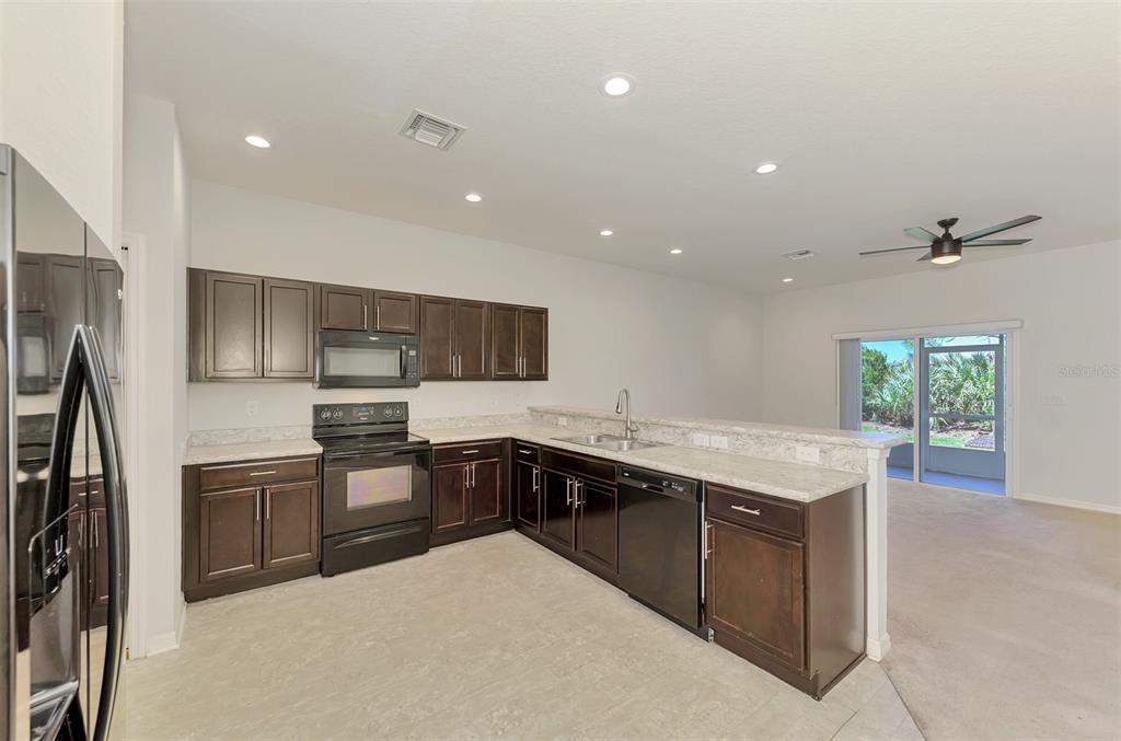 A kitchen with dark wood cabinets, light countertops, and stainless steel appliances opens to a living area — 4745 VIGNETTE WAY, SARASOTA, FL