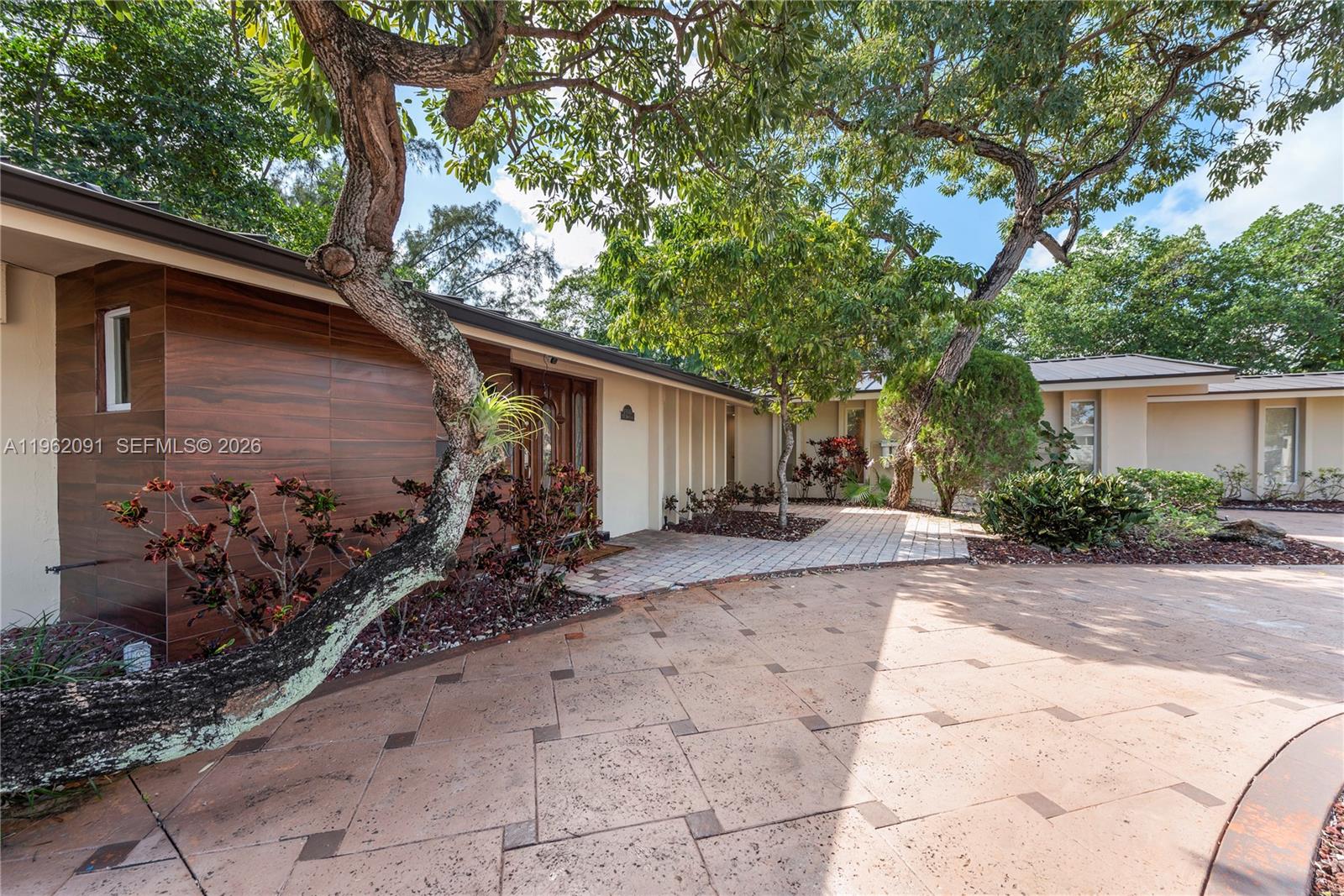 A paved driveway leads to the entrance of a house with wood-paneled exterior walls — 19860 NE 24th Ct, Miami FL 33180, MIAMI, FL