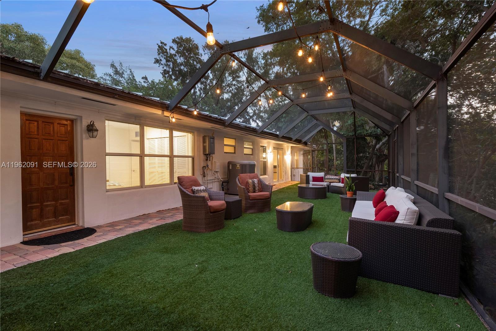 A screened-in patio features artificial turf, outdoor furniture, and string lights under a metal frame — 19860 NE 24th Ct, Miami FL 33180, MIAMI, FL