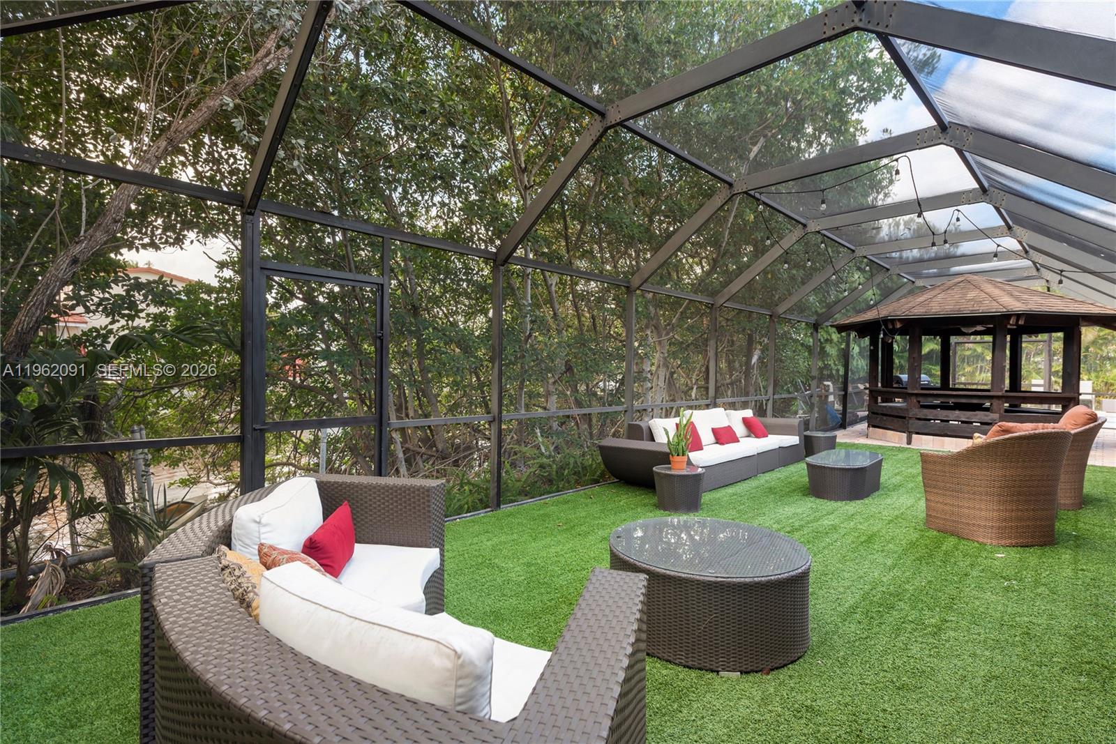 A screened-in patio features artificial turf, wicker furniture, and a gazebo in the background — 19860 NE 24th Ct, Miami FL 33180, MIAMI, FL
