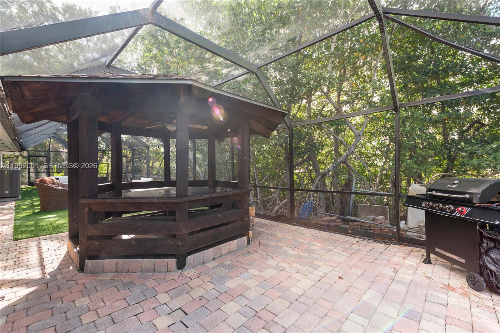 A screened-in patio features a wooden gazebo, brick pavers, and a black gas grill — 19860 NE 24th Ct, Miami FL 33180, MIAMI, FL