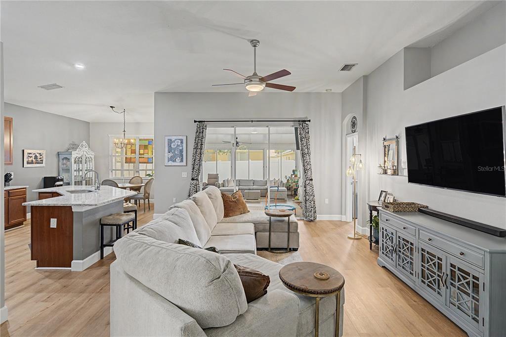 A living room with a sectional sofa, light wood flooring, and an open kitchen — 34726 PINEHURST GREENE WAY, ZEPHYRHILLS, FL