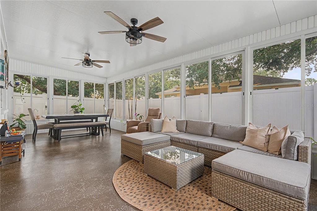 A sunroom features a dining set, a sectional sofa, two ceiling fans, and large windows — 34726 PINEHURST GREENE WAY, ZEPHYRHILLS, FL