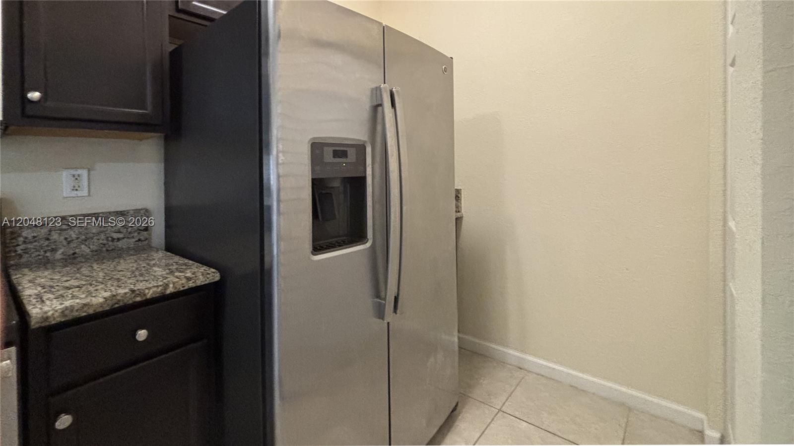 A stainless steel side-by-side refrigerator stands next to dark cabinets and granite countertops — 17170 SW 93rd St # 0, Miami FL 33196, MIAMI, FL