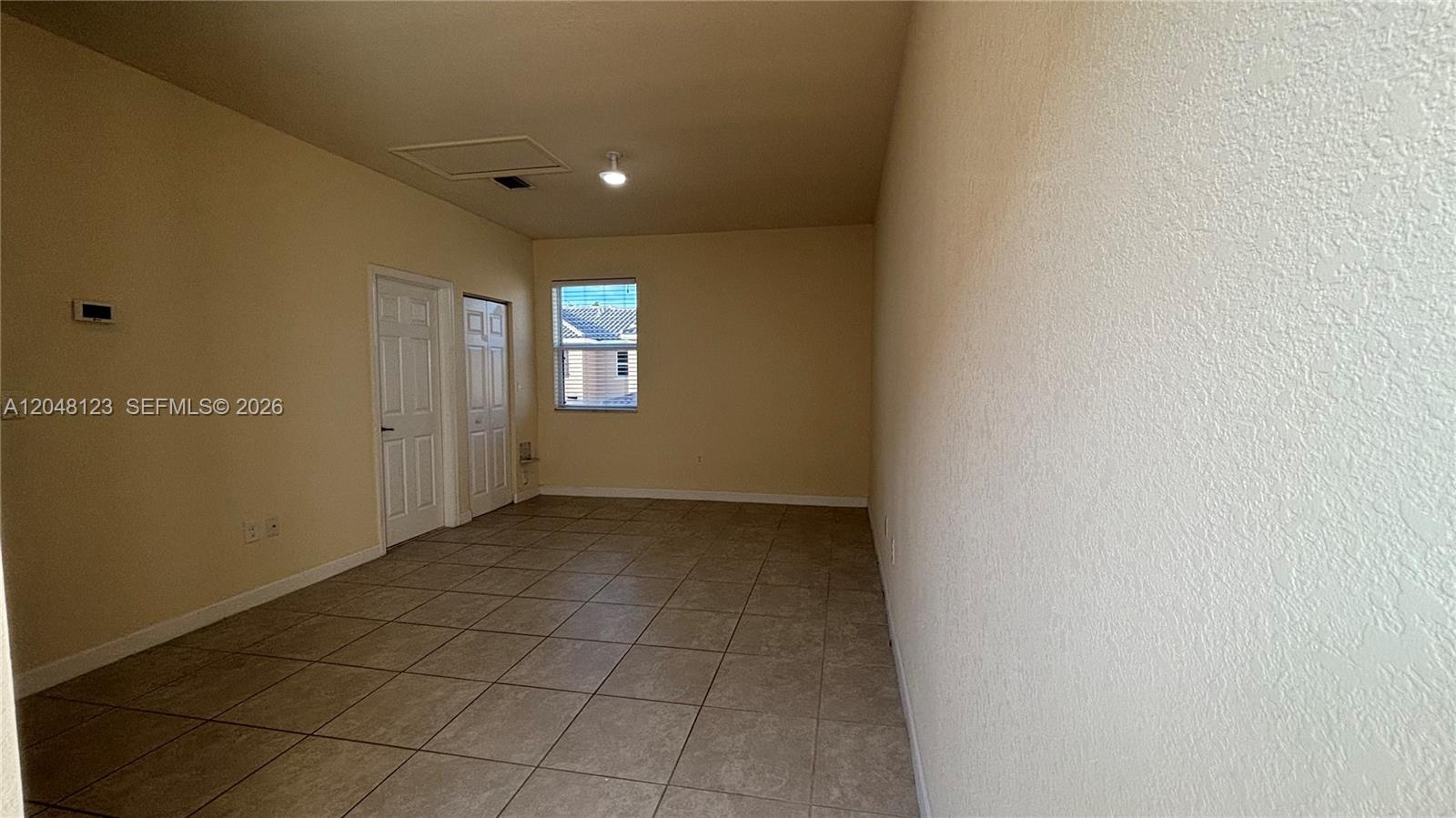 An empty room features beige walls, tiled flooring, two white doors, and a single window — 17170 SW 93rd St # 0, Miami FL 33196, MIAMI, FL