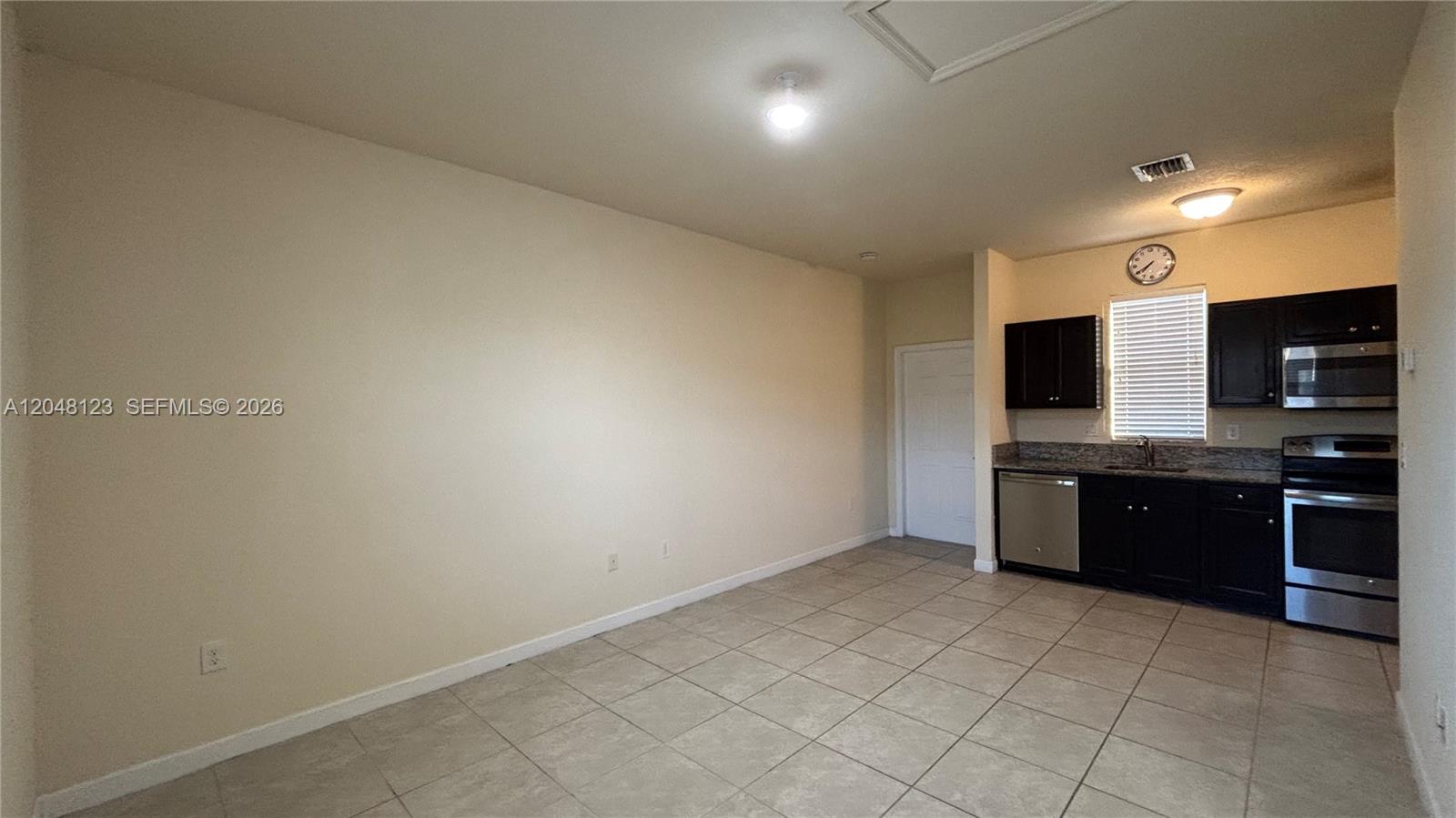 A kitchen with dark cabinets and stainless steel appliances opens into a tiled living area — 17170 SW 93rd St # 0, Miami FL 33196, MIAMI, FL