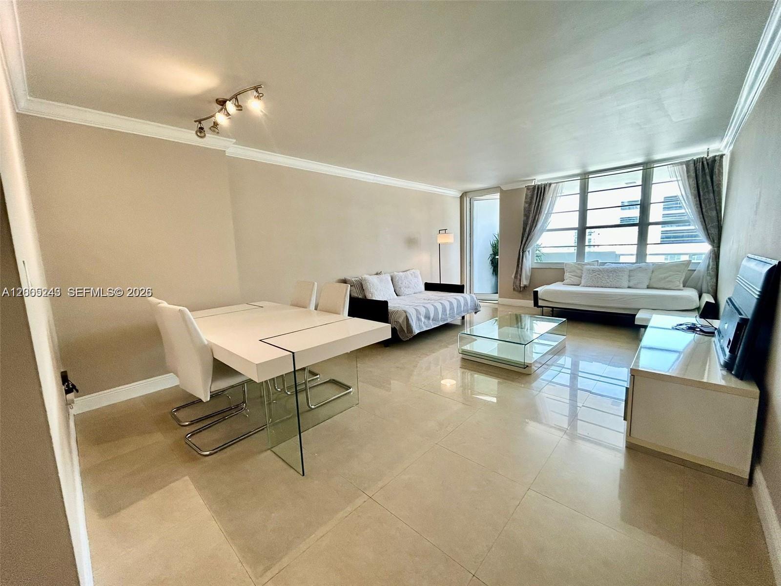 A bright living and dining area features light tile flooring and large windows with curtains — 100 Lincoln Rd # 1010, Miami Beach FL 33139, MIAMI BEACH, FL