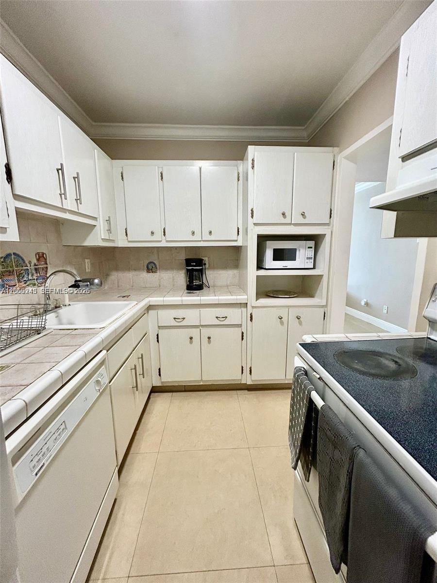 A kitchen features white cabinets, tiled countertops, a dishwasher, and a built-in microwave — 100 Lincoln Rd # 1010, Miami Beach FL 33139, MIAMI BEACH, FL