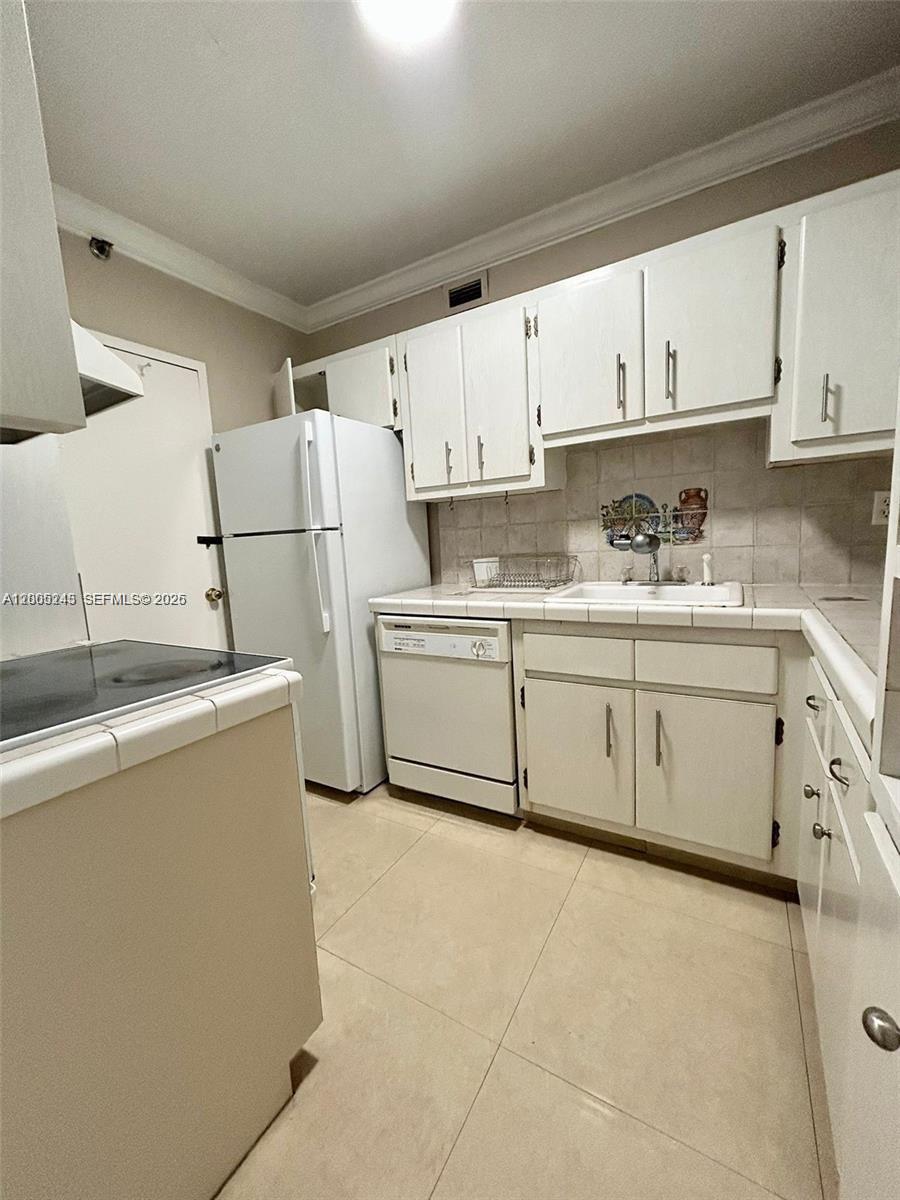 A kitchen features white cabinets, a white refrigerator, a dishwasher, and tiled countertops — 100 Lincoln Rd # 1010, Miami Beach FL 33139, MIAMI BEACH, FL