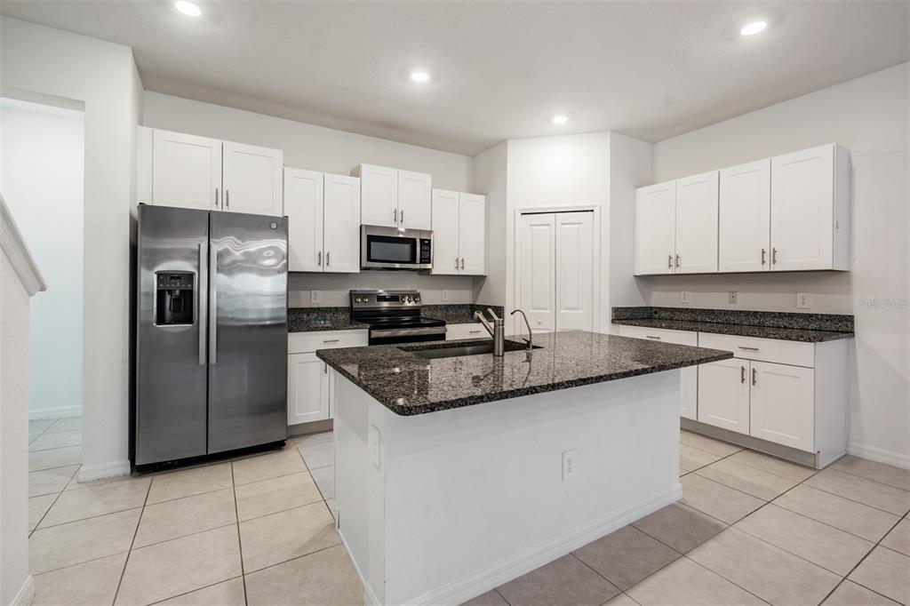 A kitchen features white cabinets, granite countertops, a center island, and stainless steel appliances — 4607 TUSCAN LOON DRIVE, TAMPA, FL
