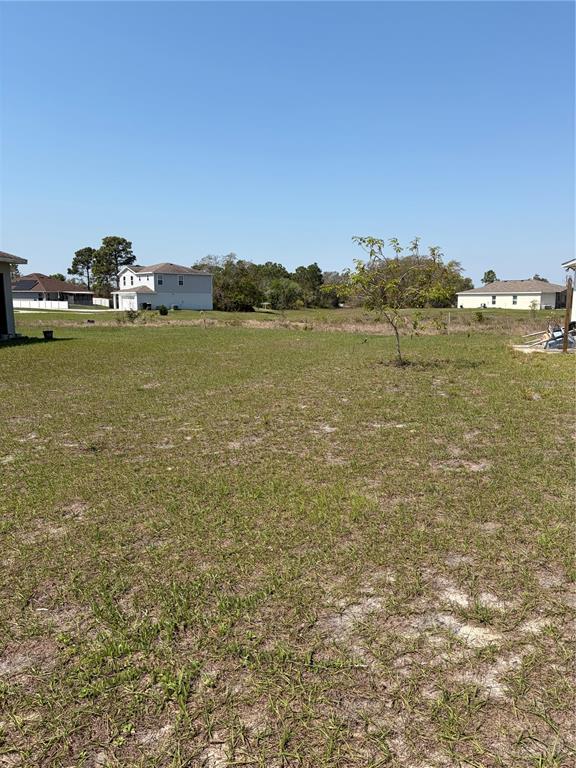 A wide, grassy vacant lot is surrounded by suburban houses under a clear blue sky — 1939 MANATEE DRIVE, KISSIMMEE, FL