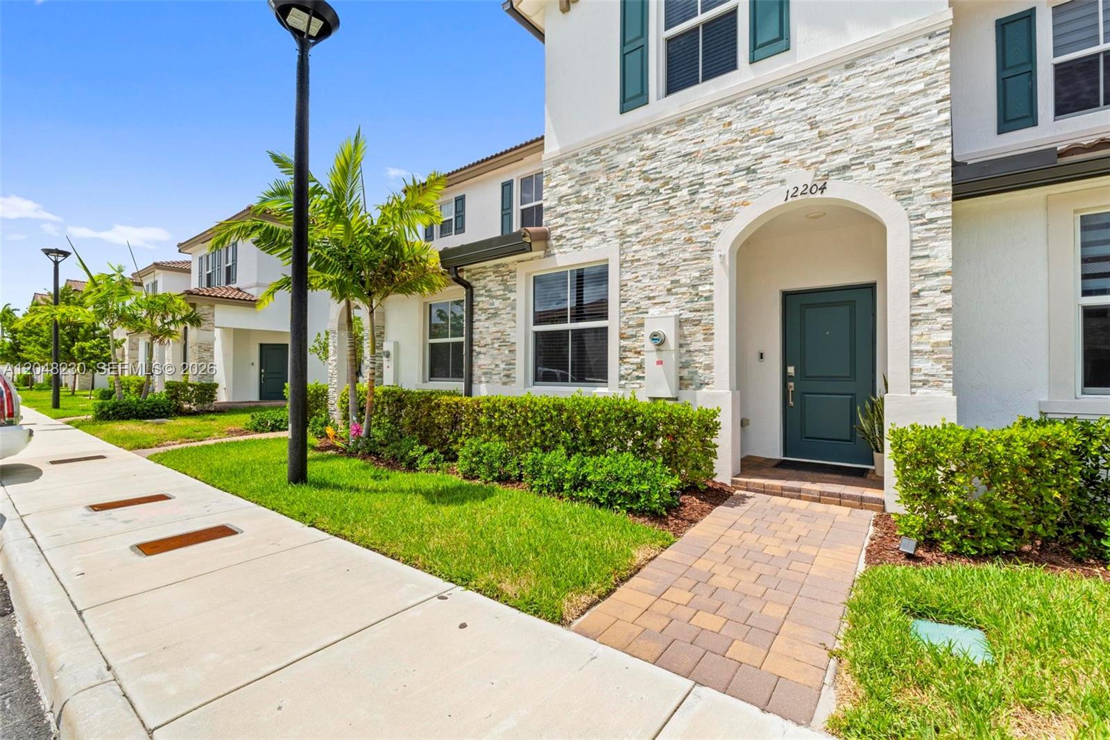 A two-story residential building features a stone facade, a dark green front door, and a walkway — 12204 NW 23rd Ct, Miami FL 33167, MIAMI, FL