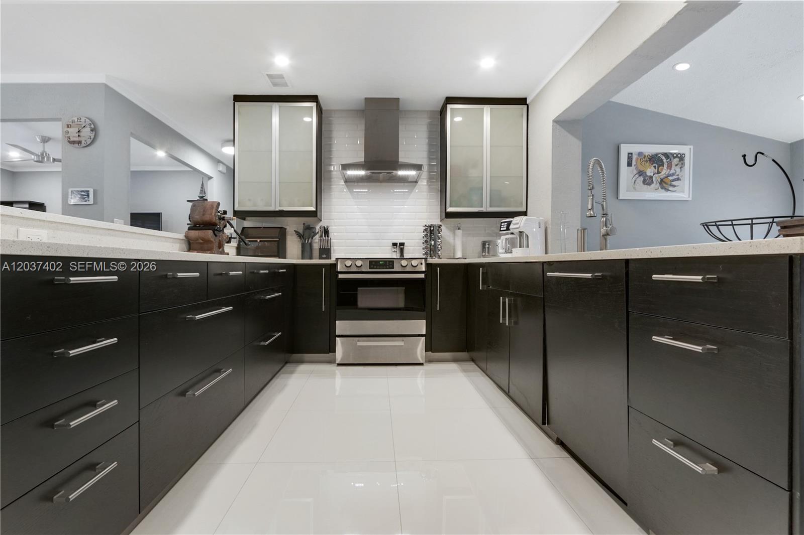 A modern kitchen features dark wood cabinetry, stainless steel appliances, and white tile flooring — 424 NE 27th Dr, Wilton Manors FL 33334, WILTON MANORS, FL