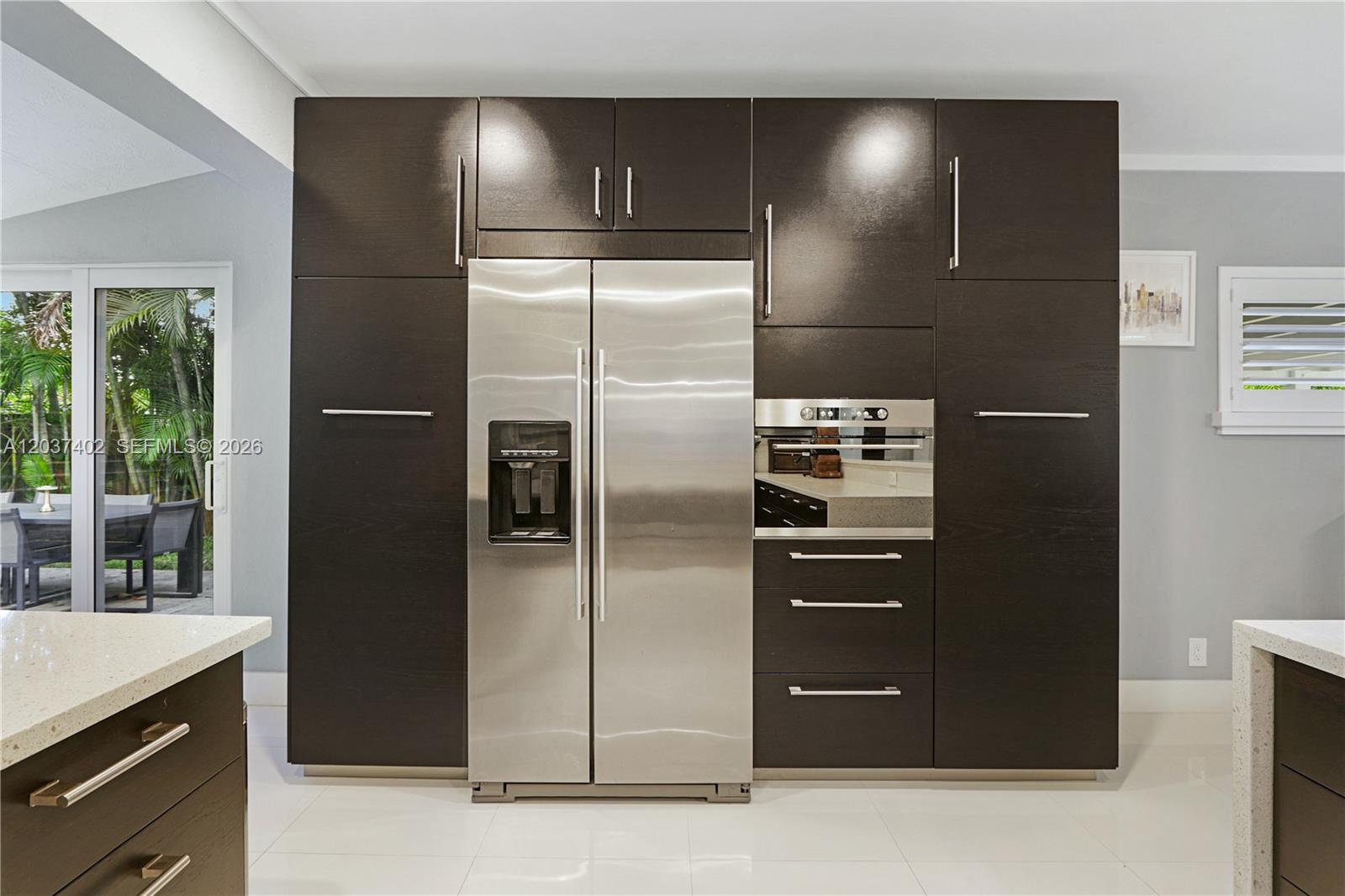 A modern kitchen features dark wood cabinetry surrounding a stainless steel refrigerator and built-in oven — 424 NE 27th Dr, Wilton Manors FL 33334, WILTON MANORS, FL