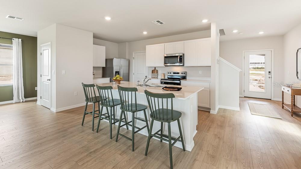 A kitchen features white cabinets, a central island with green stools, and light wood flooring — 11864 TEXOMA COURT, PARRISH, FL