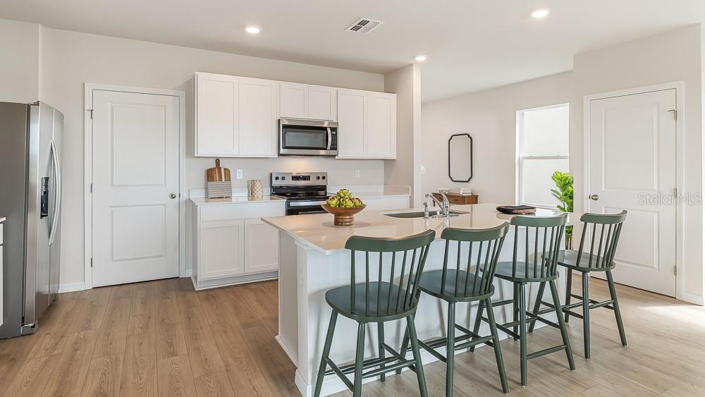 A kitchen features white cabinets, a central island with green chairs, and light wood flooring — 11864 TEXOMA COURT, PARRISH, FL