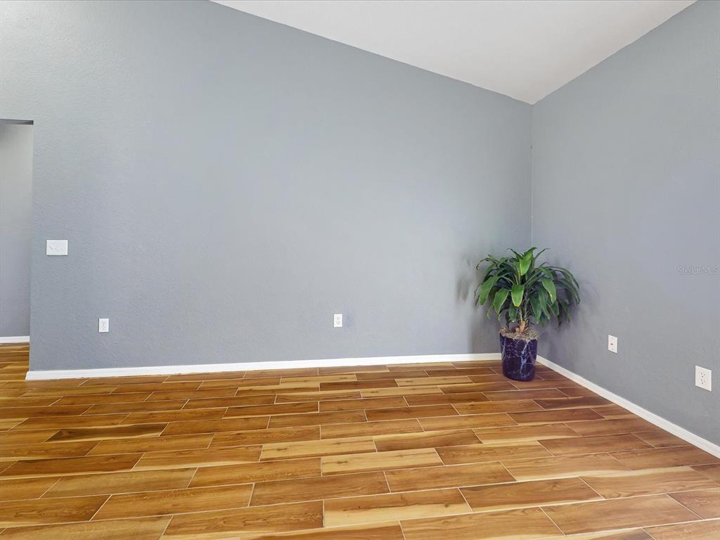 An empty room features gray walls, wood-look tile flooring, and a potted plant in the corner — 1444 SWIFT COURT, POINCIANA, FL