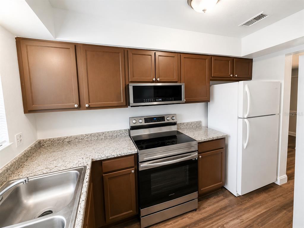 A kitchen features brown cabinets, granite countertops, stainless steel appliances, and a white refrigerator — 202 EDEN LANE UNIT B, KISSIMMEE, FL