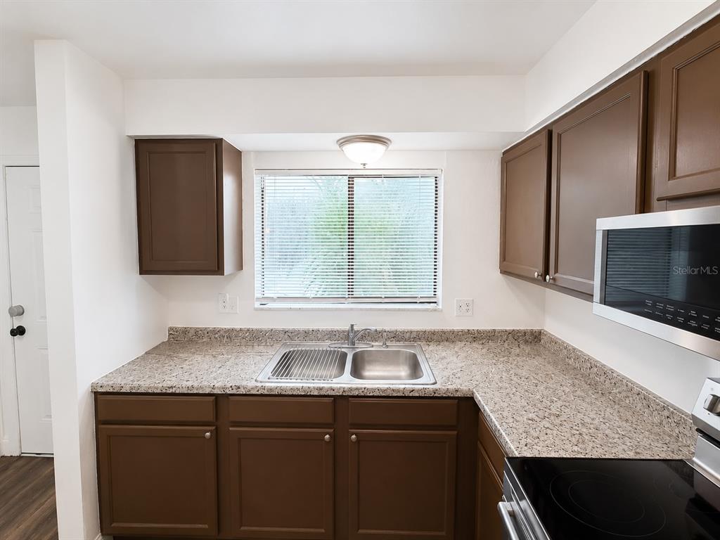 A kitchen features brown cabinets, granite countertops, a stainless steel sink, and a microwave — 202 EDEN LANE UNIT B, KISSIMMEE, FL