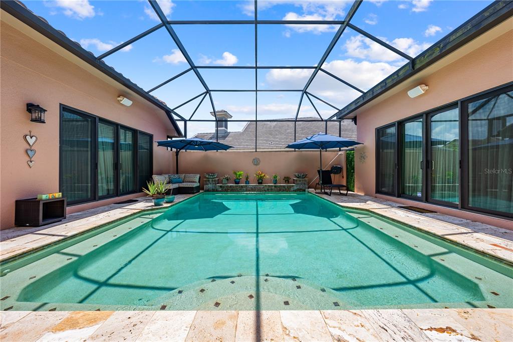 A screened-in patio features a rectangular swimming pool with stone decking and two umbrellas — 2557 HERITAGE GREEN AVENUE, DAVENPORT, FL