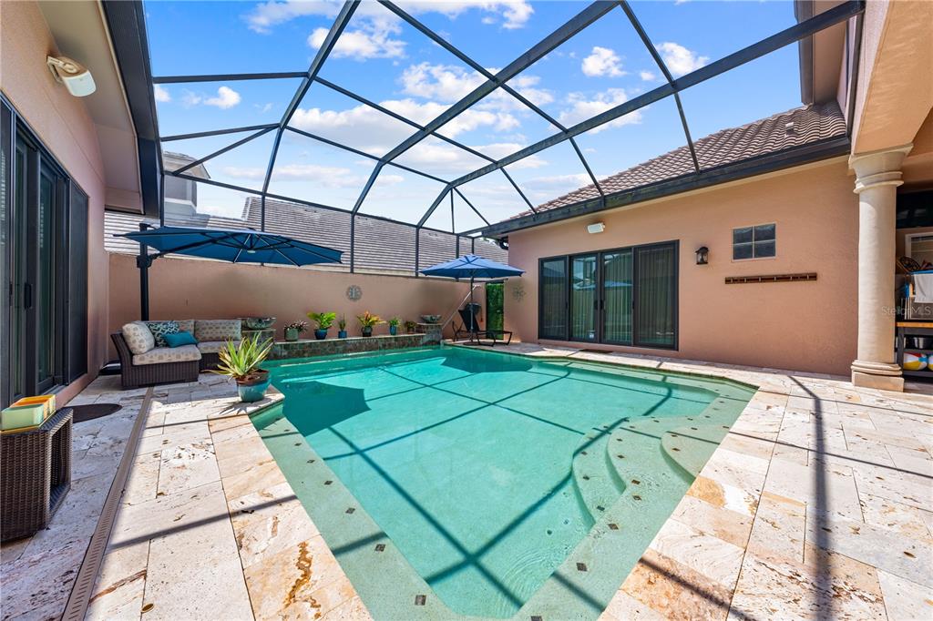 A screened-in swimming pool patio features stone tile flooring, a seating area, and potted plants — 2557 HERITAGE GREEN AVENUE, DAVENPORT, FL
