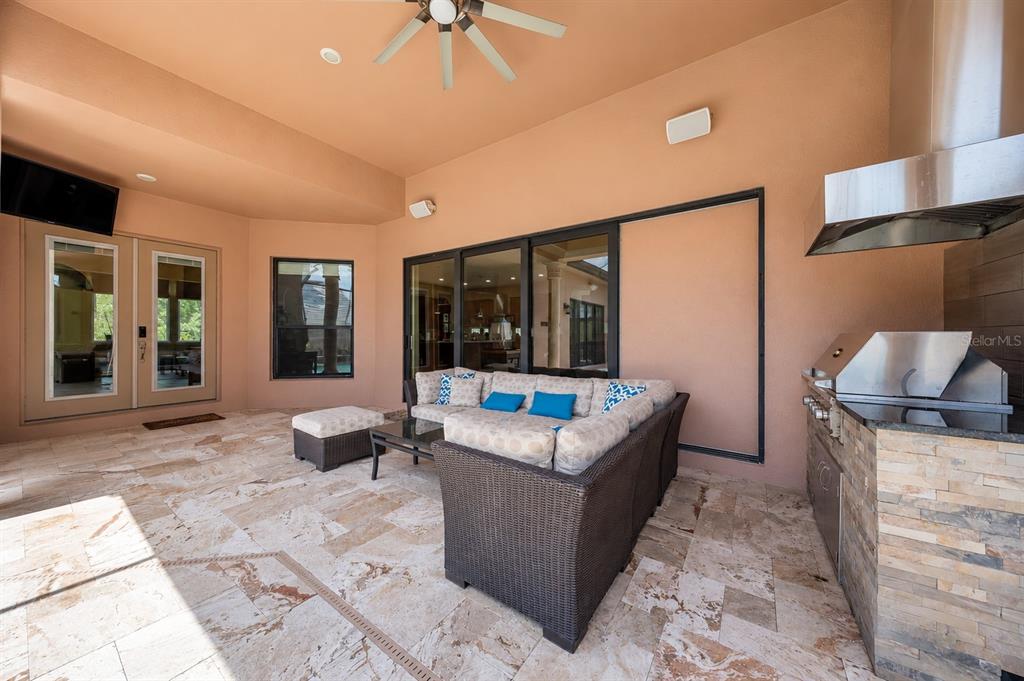 A covered outdoor patio features a stone-tiled floor, a sectional sofa, and a built-in grill — 2557 HERITAGE GREEN AVENUE, DAVENPORT, FL