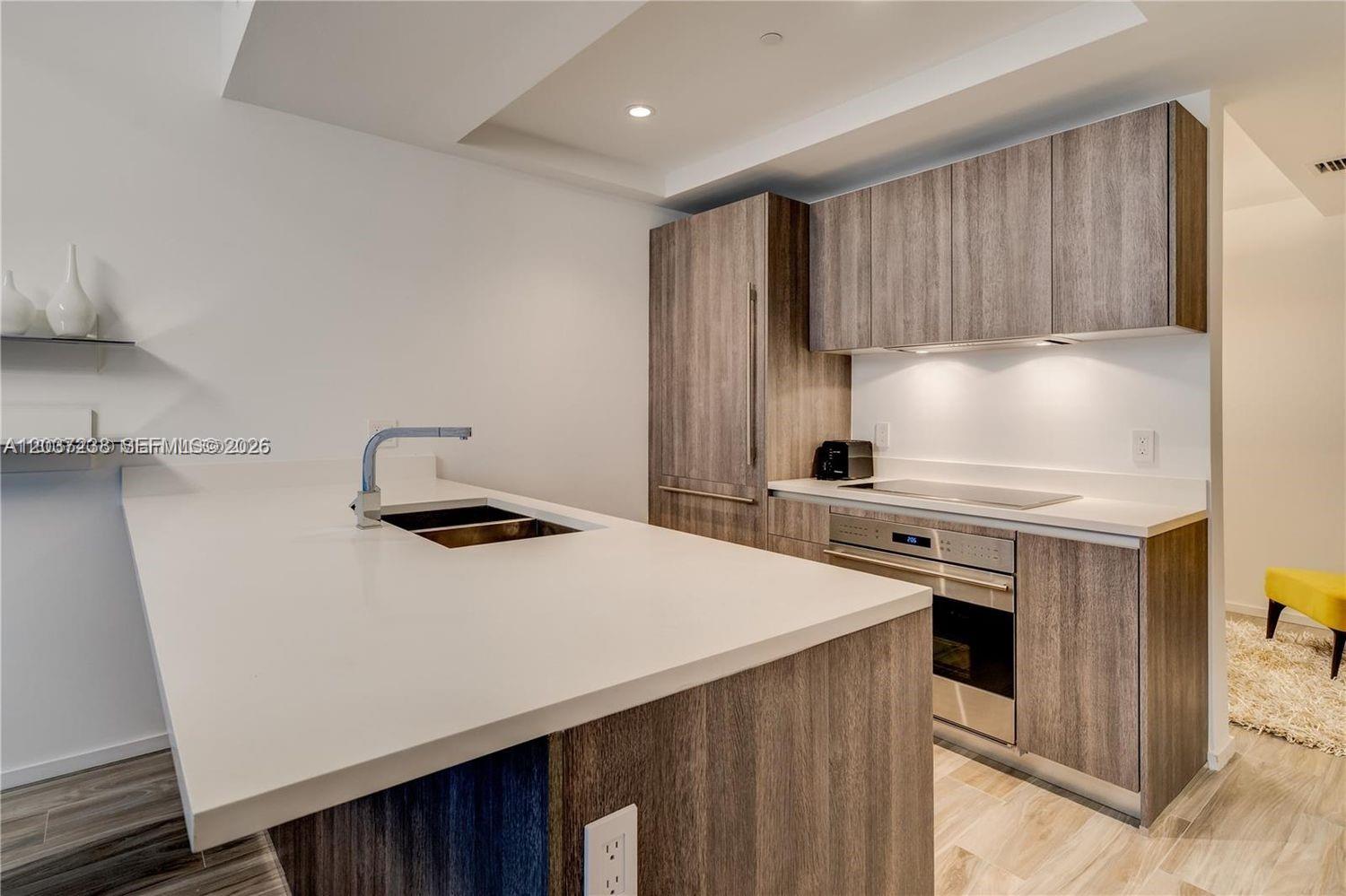 A modern kitchen features wood-grain cabinetry, a white countertop island with a sink, and stainless-steel appliances — 801 S Miami Ave # 2906, Miami FL 33130, MIAMI, FL