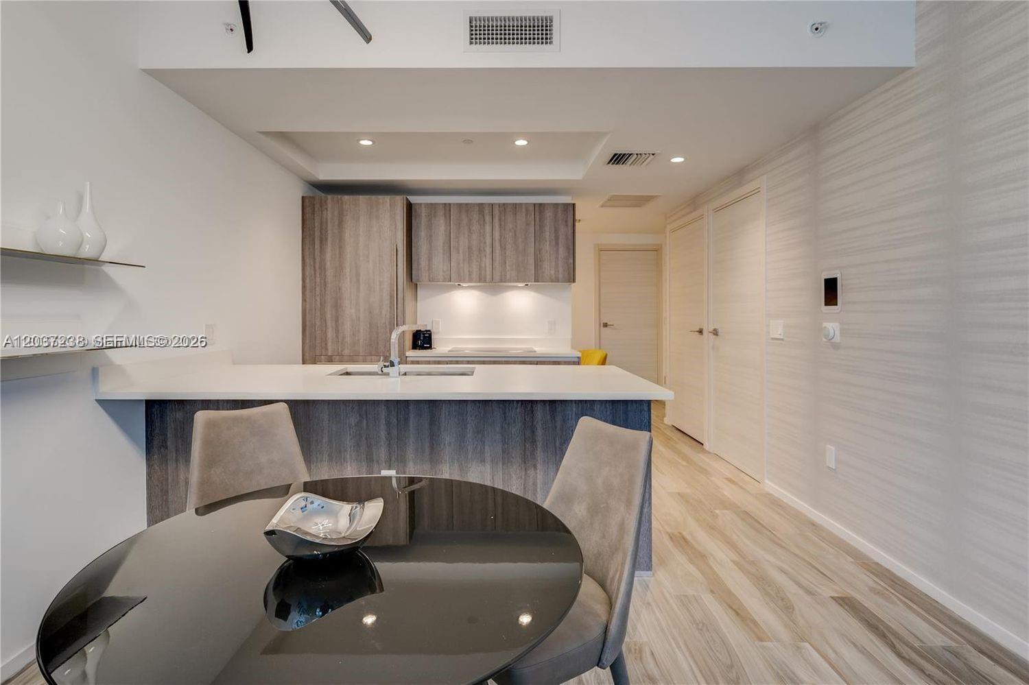 A modern kitchen features a white island, wood-toned cabinetry, and a round dining table — 801 S Miami Ave # 2906, Miami FL 33130, MIAMI, FL