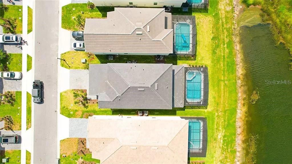An aerial view shows three houses with screened-in pools along a body of water — 7243 OAKMOSS LOOP, DAVENPORT, FL