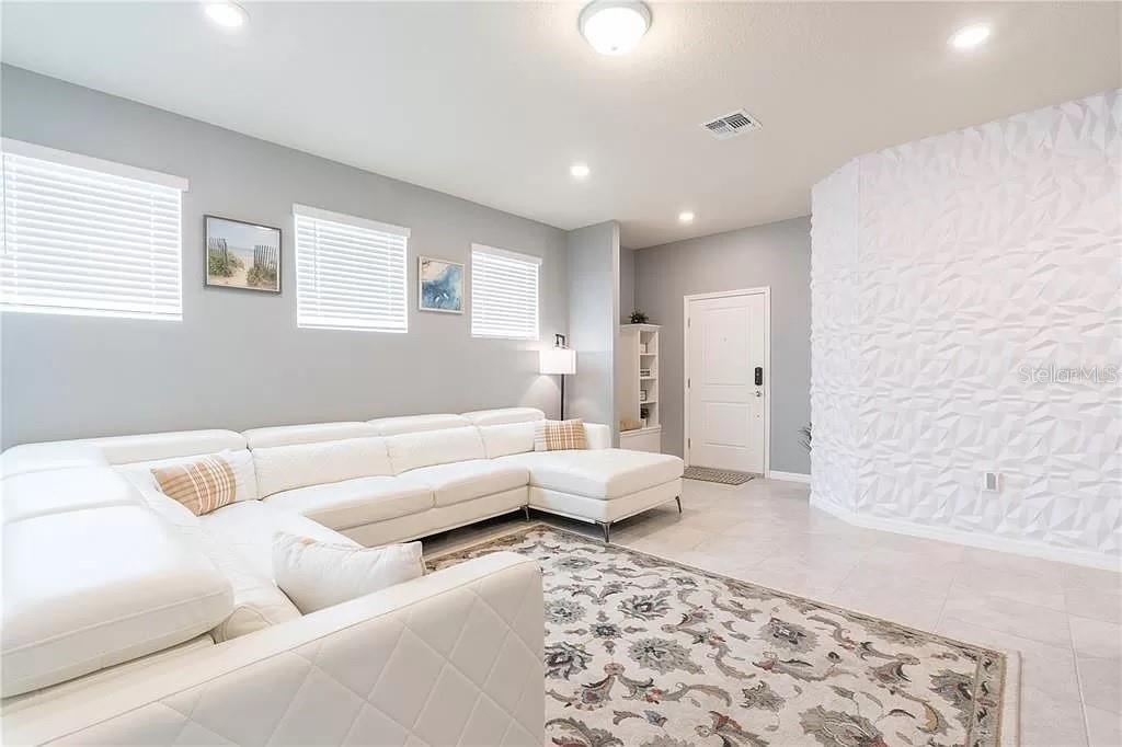 A living room features a white sectional sofa, a patterned area rug, and textured wall paneling — 7243 OAKMOSS LOOP, DAVENPORT, FL