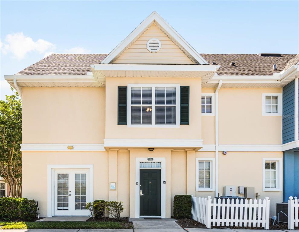 A two-story townhouse exterior with beige siding, a dark front door, and a white fence — 2200 SAN ZANOBI DRIVE UNIT 108, KISSIMMEE, FL