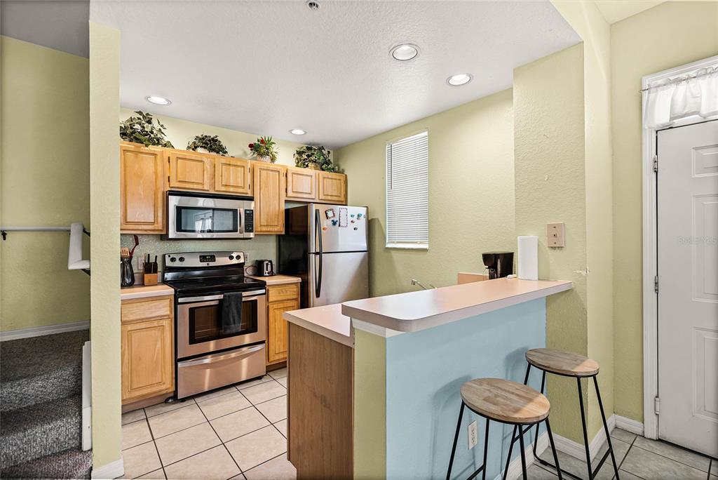 A kitchen with light wood cabinets, stainless steel appliances, a breakfast bar, and tile flooring — 2200 SAN ZANOBI DRIVE UNIT 108, KISSIMMEE, FL