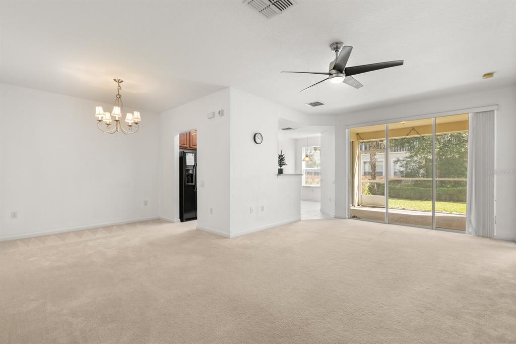 A spacious living and dining area with beige carpeting, a ceiling fan, and sliding glass doors — 409 HILGARD COVE UNIT 106, SANFORD, FL