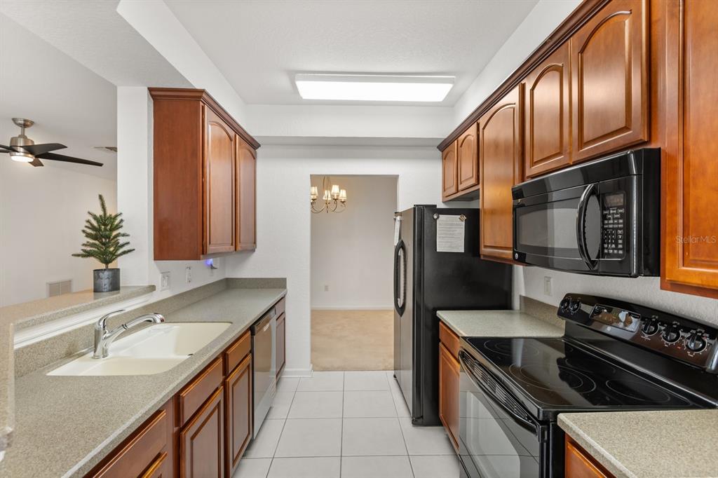A galley kitchen features wood cabinets, black appliances, and light-colored countertops — 409 HILGARD COVE UNIT 106, SANFORD, FL