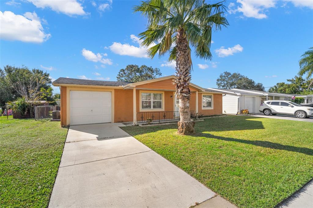 A single-story house with an orange exterior, a concrete driveway, and a palm tree — 4642 EASTWOOD LANE, HOLIDAY, FL