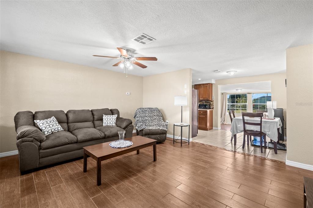 A living room with wood-look tile flooring, a brown sofa, and an adjacent dining area — 4642 EASTWOOD LANE, HOLIDAY, FL