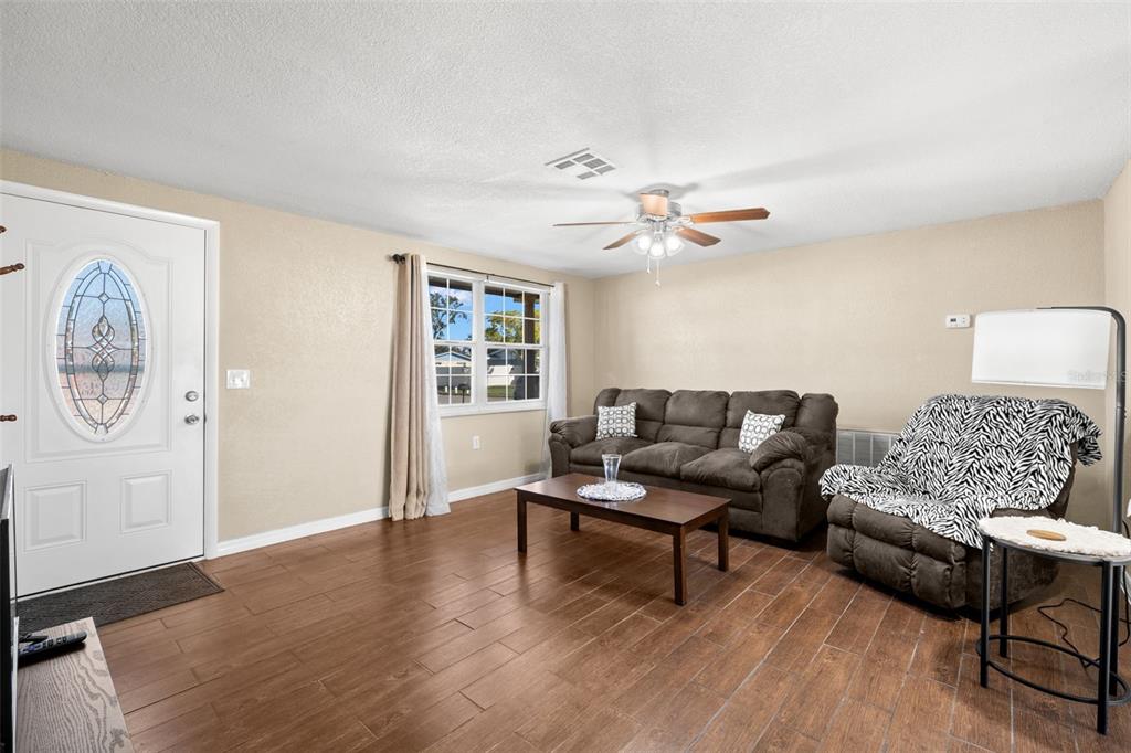 A living room features wood-look tile flooring, a brown sofa, and a recliner with a zebra-print cover — 4642 EASTWOOD LANE, HOLIDAY, FL