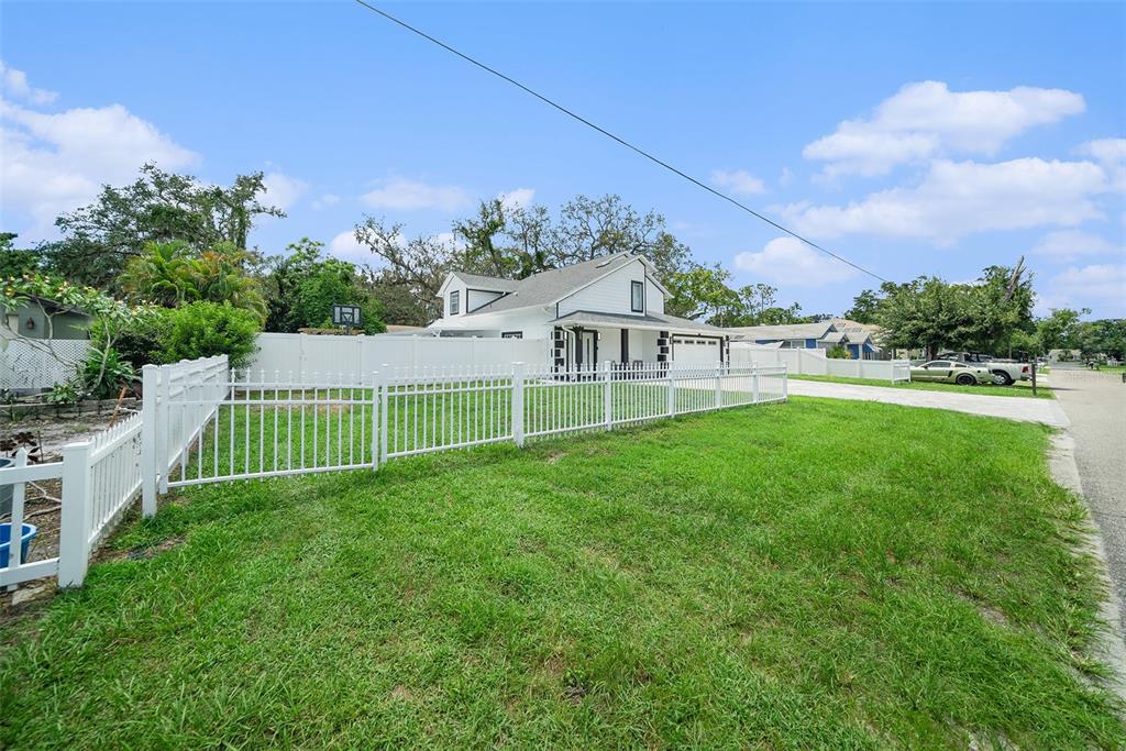 A white house with a fenced yard and a driveway sits under a blue sky — 8502 MAY STREET, TAMPA, FL