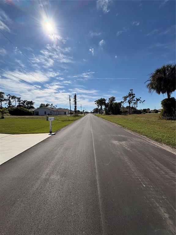 A paved road stretches into the distance under a bright blue sky with scattered clouds — 263 BROADMOOR LANE, ROTONDA WEST, FL