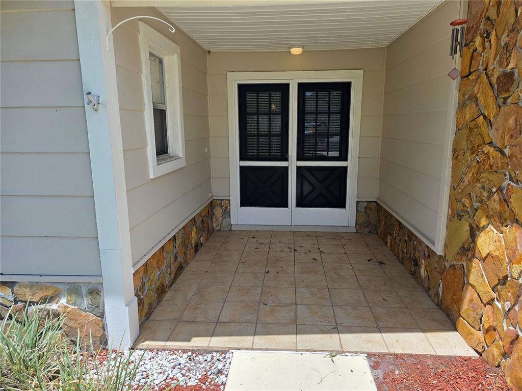 A covered porch features tiled flooring, stone accents, and a double screen door entrance — 6234 GLEN EAGLES COURT, SPRING HILL, FL