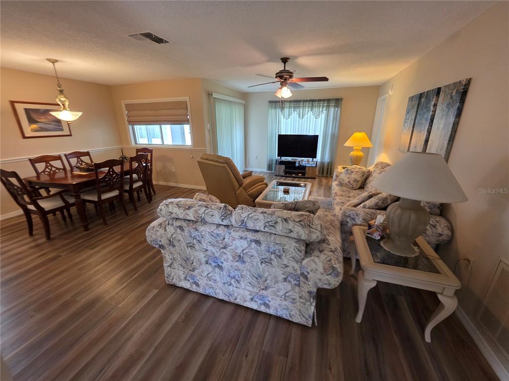 A living and dining room area features floral sofas, wood-look flooring, and a ceiling fan — 6234 GLEN EAGLES COURT, SPRING HILL, FL