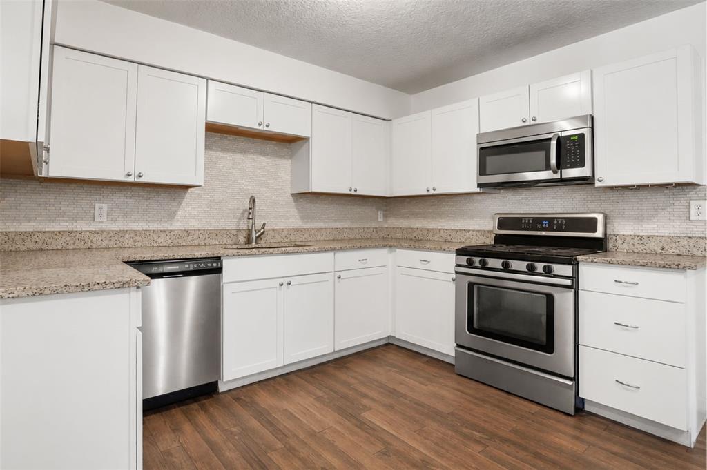 A kitchen features white cabinets, stainless steel appliances, granite countertops, and wood-look flooring — 1124 GRANT AVENUE, MOUNT DORA, FL