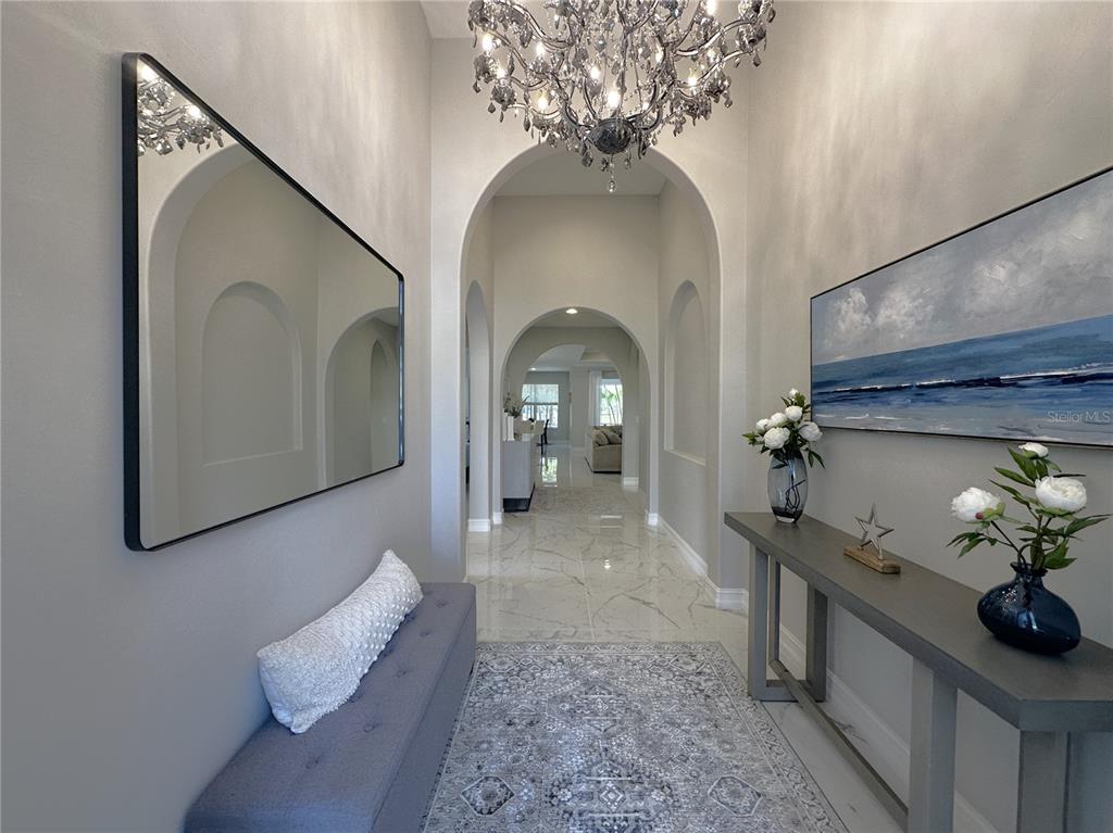 A bright entryway features a crystal chandelier, arched doorways, marble floors, and a console table — 25191 KEYGRASS COURT, PUNTA GORDA, FL