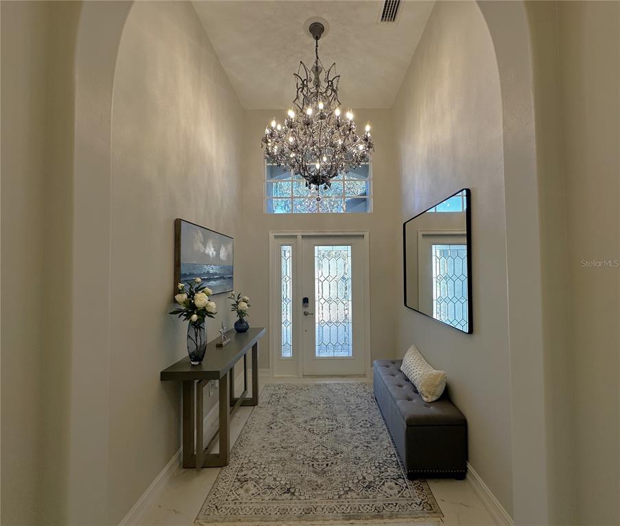 A bright entryway features a crystal chandelier, a console table, a bench, and a rug — 25191 KEYGRASS COURT, PUNTA GORDA, FL
