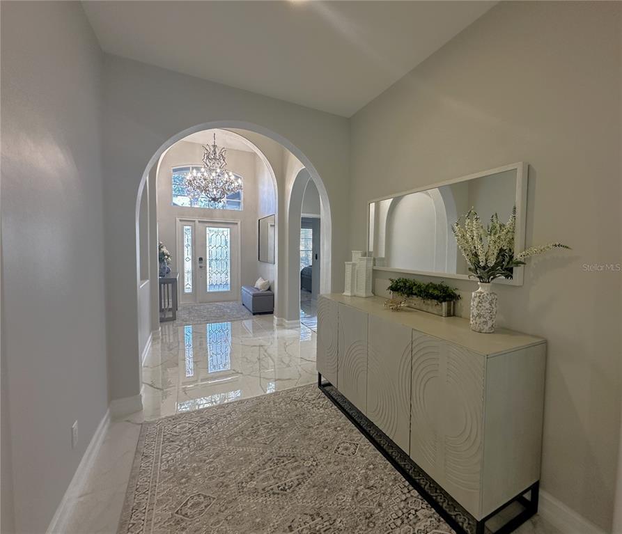 An entryway features arched doorways, marble-look tile flooring, a chandelier, and a modern console table — 25191 KEYGRASS COURT, PUNTA GORDA, FL
