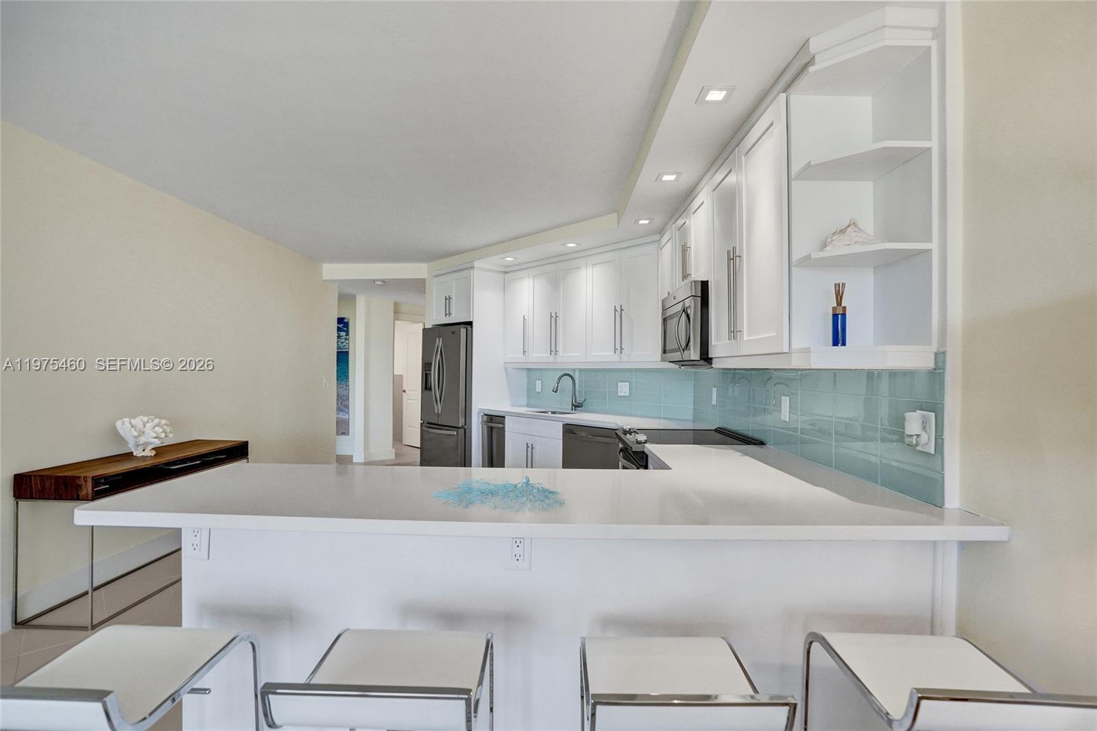 A modern kitchen features white cabinetry, a light blue backsplash, and a breakfast bar — 1936 S Ocean # 21D, Hallandale Beach FL 33009, HALLANDALE BEACH, FL