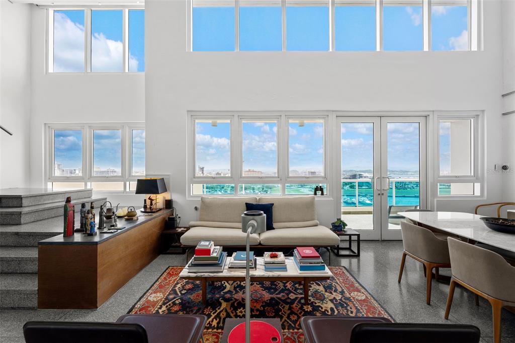 A bright, double-height living room features large windows, a beige sofa, and a patterned rug — 550 AVENIDA CONSTITUCION UNIT PH-1608, SAN JUAN, PR