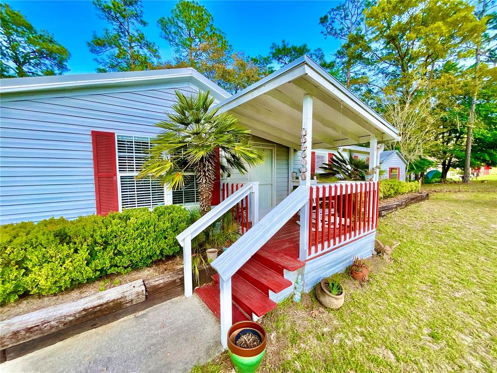 A light blue house features a red-railed front porch with wooden steps and landscaping — 129 CRYSTAL LAKE DRIVE, MELROSE, FL