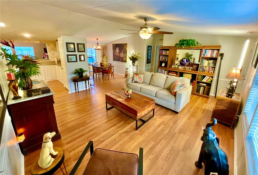 A living room with wood-look flooring, a beige sofa, and an open-concept dining area — 129 CRYSTAL LAKE DRIVE, MELROSE, FL